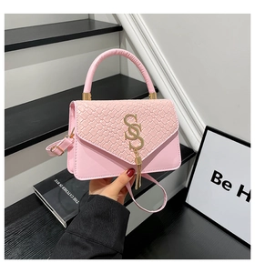Detalle del bolso bandolera rosa con textura tejida, hebilla S dorada y colgante de borla