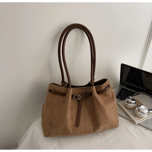 Detail of camel suede tote bag with brown leather handles and metallic buckle on desk