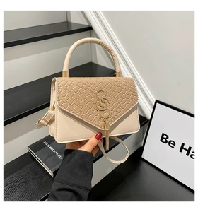 Detail of beige woven leather flap bag featuring gold interlocking logo and metal tassel