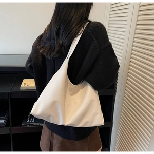 Close-up of white large capacity tote bag worn on shoulder by model in minimalist setting