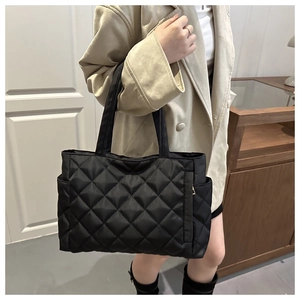 Detail of black quilted tote bag with side pocket and sleek nylon texture on model