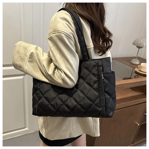 Detail of black quilted tote bag showing side zipper pocket and large capacity on model