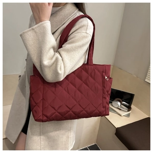 Detail of burgundy quilted tote bag featuring diamond stitching and side zipper pocket