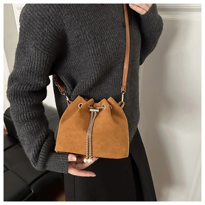 Detailed view of brown suede bucket bag with metal chain and pearl charm detail