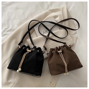 Detail of matte suede drawstring bucket bags in black and brown with pearl chain straps