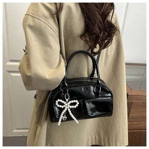 Detail of black patent leather crossbody bag with pearl bow charm and heart pendant