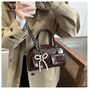 Detail of dark brown faux leather underarm bag with beaded bow pendant and dual pockets