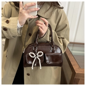 Chocolate patent leather Boston bag with pearl bow charm styled with a trench coat