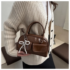 Brown glossy leather crossbody bag detail with twin pockets and pearl bow pendant