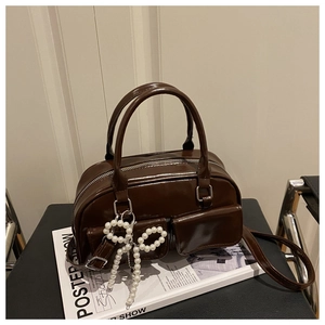 Brown gloss Boston bag with pearl bow charm and dual front pockets on a black chair