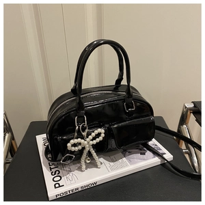 Detail of glossy black patent leather Boston bag with decorative pearl bow charm