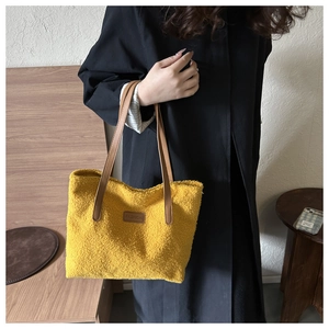 Close-up of a yellow faux shearling tote bag with leather handles and Fashion patch