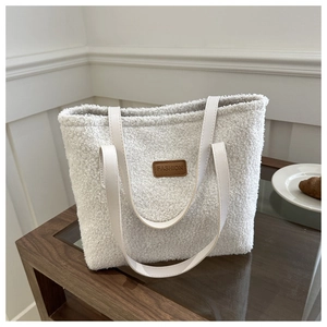 Detail shot of white fuzzy tote bag with leather straps and Fashion label on wood