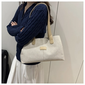 Détail d'un cabas en toile montrant la texture crème et la bandoulière en cuir sur l'épaule