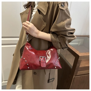 Detail of red distressed leather tote bag with silver studs worn with khaki trench coat
