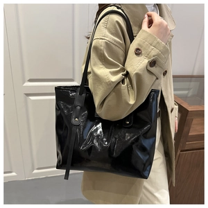 Detail of glossy black patent leather tote bag with long decorative shoulder straps