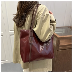 Macro detail of glossy wine red tote bag with slim brown shoulder straps on model
