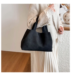 Detail of a black suede bucket bag styled with a white tweed jacket for a chic winter look