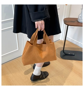 Detail of a brown suede tote bag with a soft matte finish and wide handles