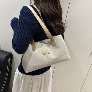 Minimalist beige canvas tote bag with khaki leather handles shown on a model's shoulder