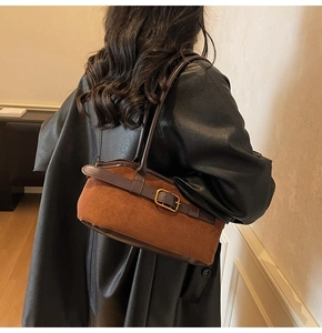 Brown suede underarm bag with gold buckle shown on model wearing black leather jacket
