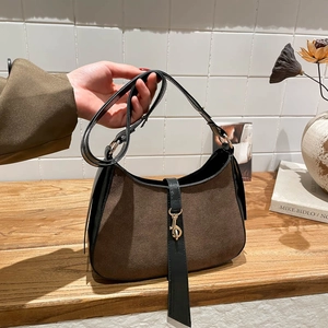 Detail of a brown suede baguette bag with black leather trim and gold metal clasp