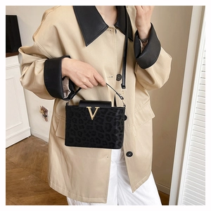 Détail d'un sac à main léopard avec boucle dorée en V porté par un mannequin en salle