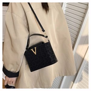 Détail du sac à main noir léopard avec boucle en V dorée porté sur un trench-coat beige