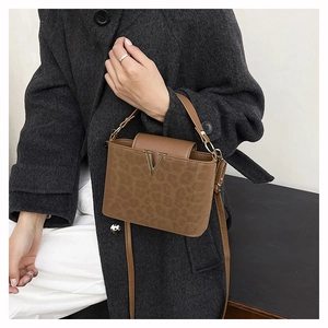 Détail du sac léopard avec boucle en V métallique porté sur un manteau en laine gris