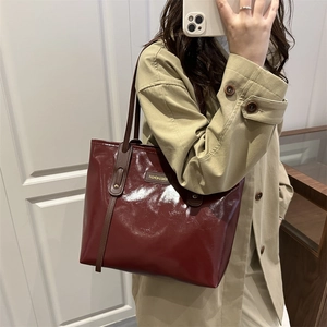 Deep red patent leather tote bag with brown handles and gold rivets on a model