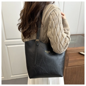 Detailed view of black PU leather tote bag with gold hardware and logo on model