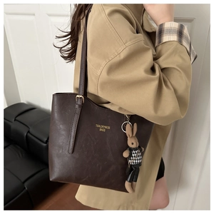 Detail view of dark brown tote bag texture with golden logo and cute rabbit charm