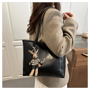 Detail of black faux leather tote bag featuring a cute bunny plush charm on the strap