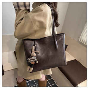 Detail of dark brown tote bag featuring a cute knitted rabbit charm and retro leather texture