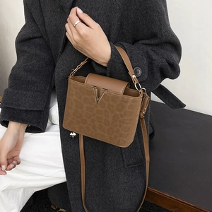Sac seau marron à imprimé léopard avec V doré porté par un mannequin en manteau gris