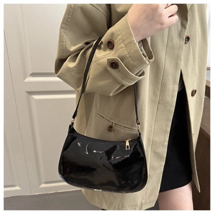 Polished black patent leather crescent underarm bag shown with a stylish trench coat