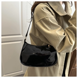 Detail of glossy black patent leather underarm bag with gold zipper on a beige coat