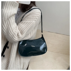 Detail of dark green patent leather shoulder bag showing glossy finish on a white cardigan