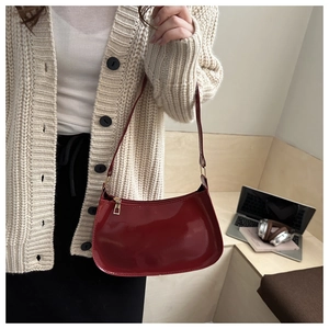 Detail of red patent leather shoulder bag with glossy finish and gold zipper on a model