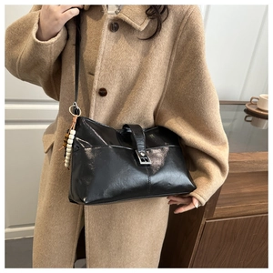 Détail du sac bandoulière noir brillant avec boucle argentée et pendentif à perles