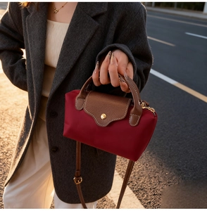 Detail of burgundy nylon crossbody bag with brown leather flap in warm outdoor setting