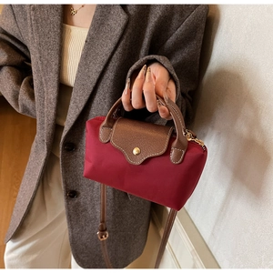 Close-up of red nylon mini crossbody bag with brown leather handles and gold snap button
