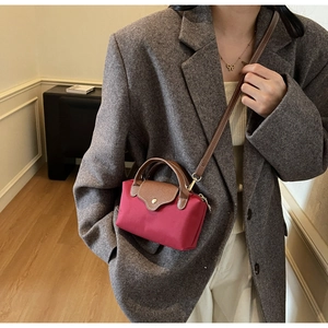 Detail of red nylon crossbody bag with brown leather flap and golden snap button closure
