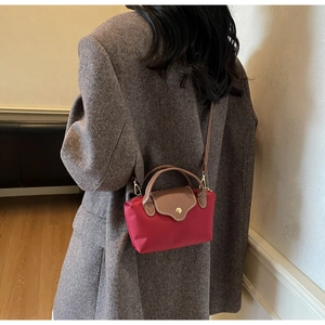 Detail of burgundy nylon mini bag with leather handles and gold clasp shown on person