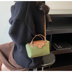 Green nylon crossbody bag with brown leather handles worn by a model in a minimal setting