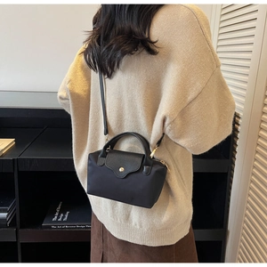 On-body shot of a black nylon mini crossbody bag with leather contrast and metal clasp