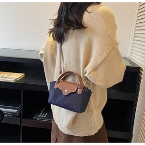 Detail of navy nylon crossbody bag with brown leather trim and golden metal snap buckle
