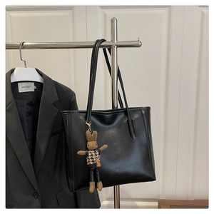 Detail of black faux leather tote bag with stylish bunny charm on a metal hanger