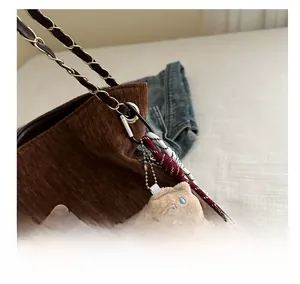 Gros plan du sac cabas en velours marron avec écusson chat et breloque ours en peluche