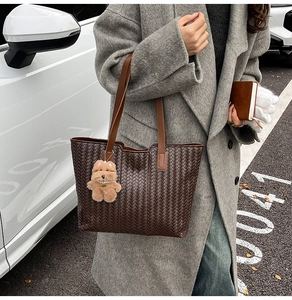 Detail of dark brown woven tote bag with plush charm on textured shoulder strap